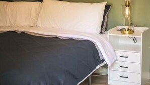Una cama con ropa de cama blanca y negra, una mesita de noche con cajones y una lámpara de pared.