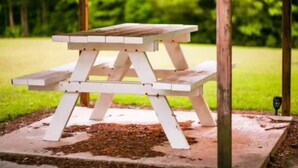 Una mesa de picnic de madera con banco, ubicada sobre una base de concreto en un área con césped.