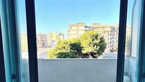 Un balcón con dos sillas de mimbre, una pared blanca y vistas a edificios y árboles.