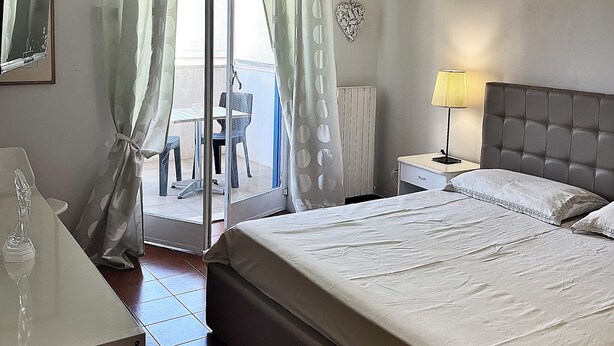 Habitación de hotel con cama, escritorio, silla, lámpara y vista al exterior.