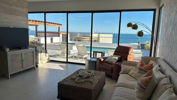 A spacious living room with a large sliding glass door leading to a balcony with a pool and ocean view. - Luxury Villa w/Ocean views, Private Pool & Hot Tub. Steps from the beach! (San Felipe)