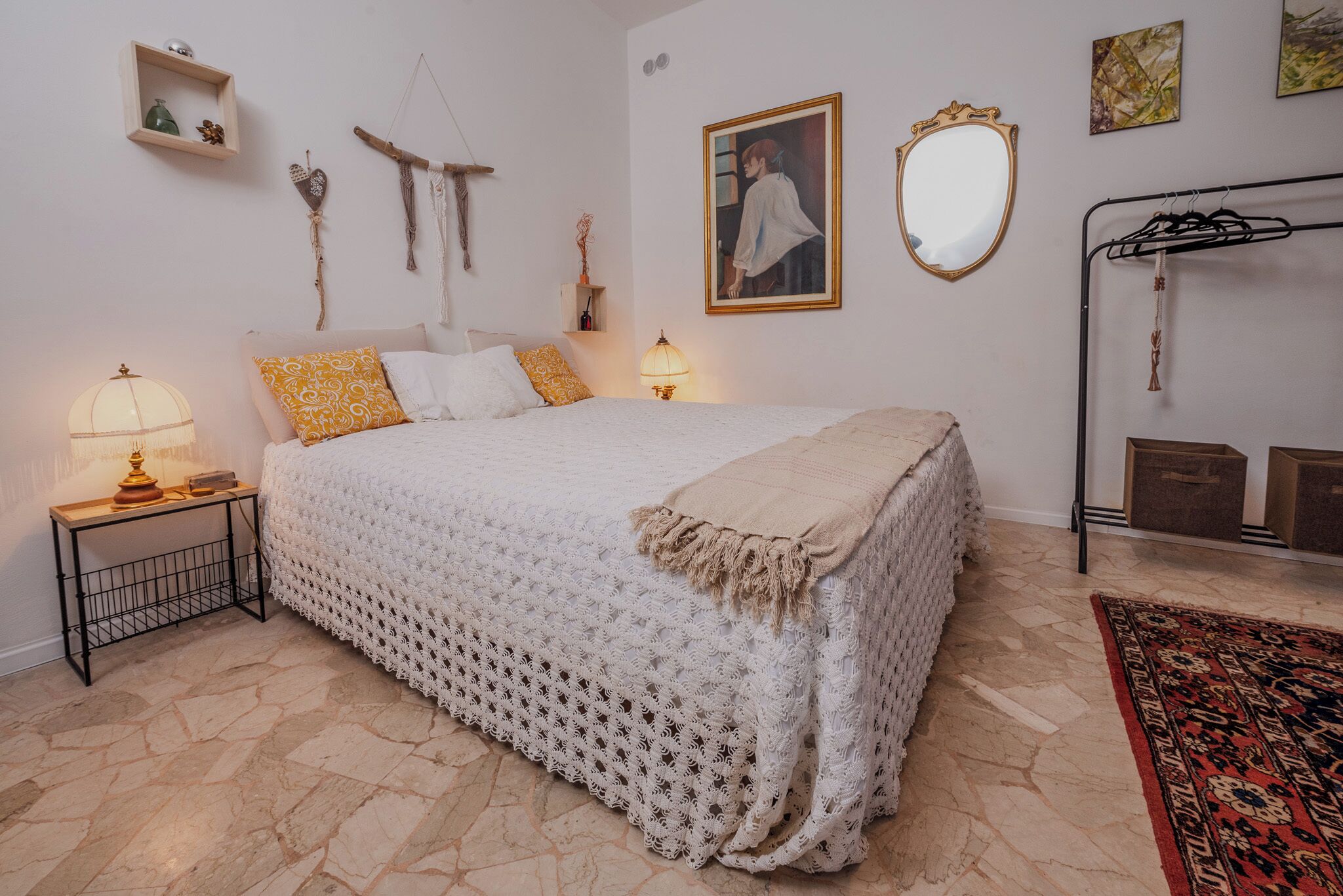 A bedroom with a large bed, bedside tables, a hanging light, a mirror, and a wall-mounted shelf.