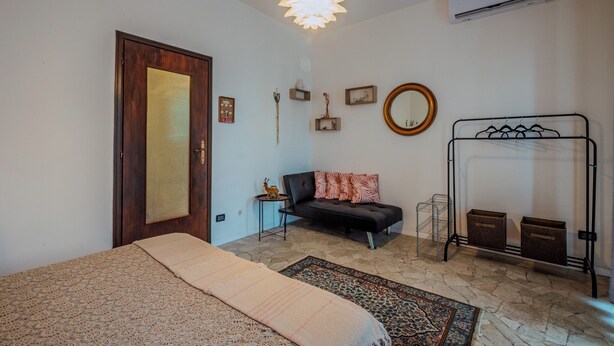 Un dormitorio con una cama, un sofá, una alfombra, una lámpara colgante, un espejo y un aire acondicionado instalado en la pared.