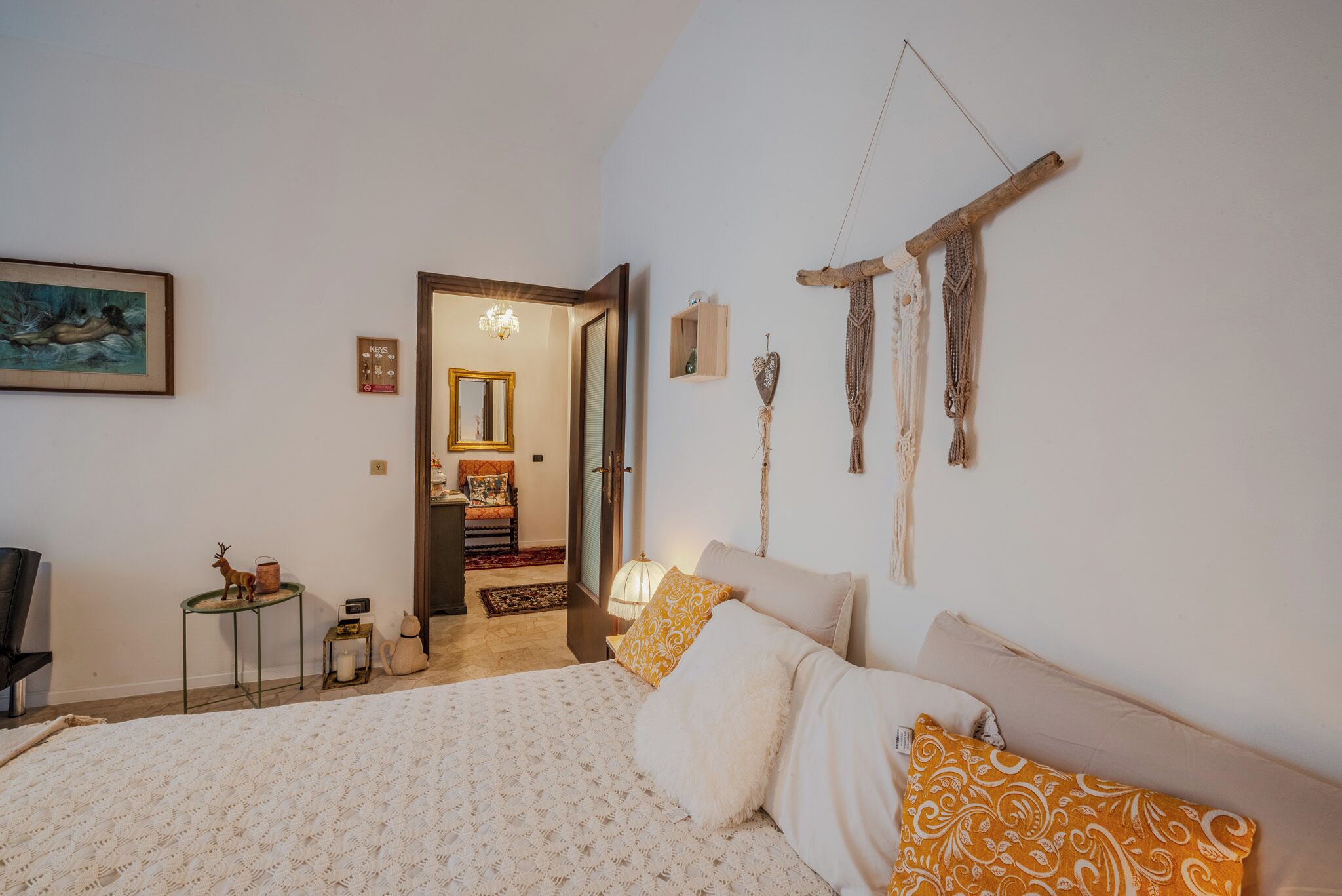 A bedroom with a bed, a chair, a small table, and a decorative macrame wall hanging.