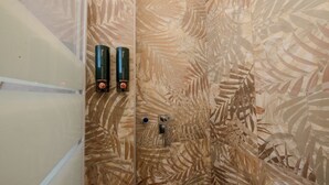 Une douche avec un mur décoré de motifs de feuilles, deux bouteilles noires et un robinet.