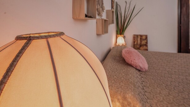 Une pièce comprenant un lit, une lampe, une petite plante et une étagère en bois ornée d’objets décoratifs.