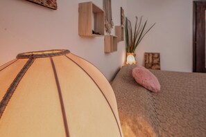Een kamer met een bed, een lamp, een klein plantje en een houten plankje met decoratieve spullen.