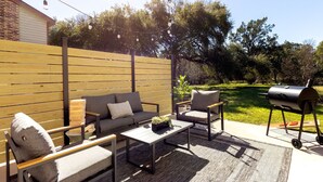 Eine Terrasse im Freien mit einer Couch, Stühlen, einem Tisch und einem Grill.