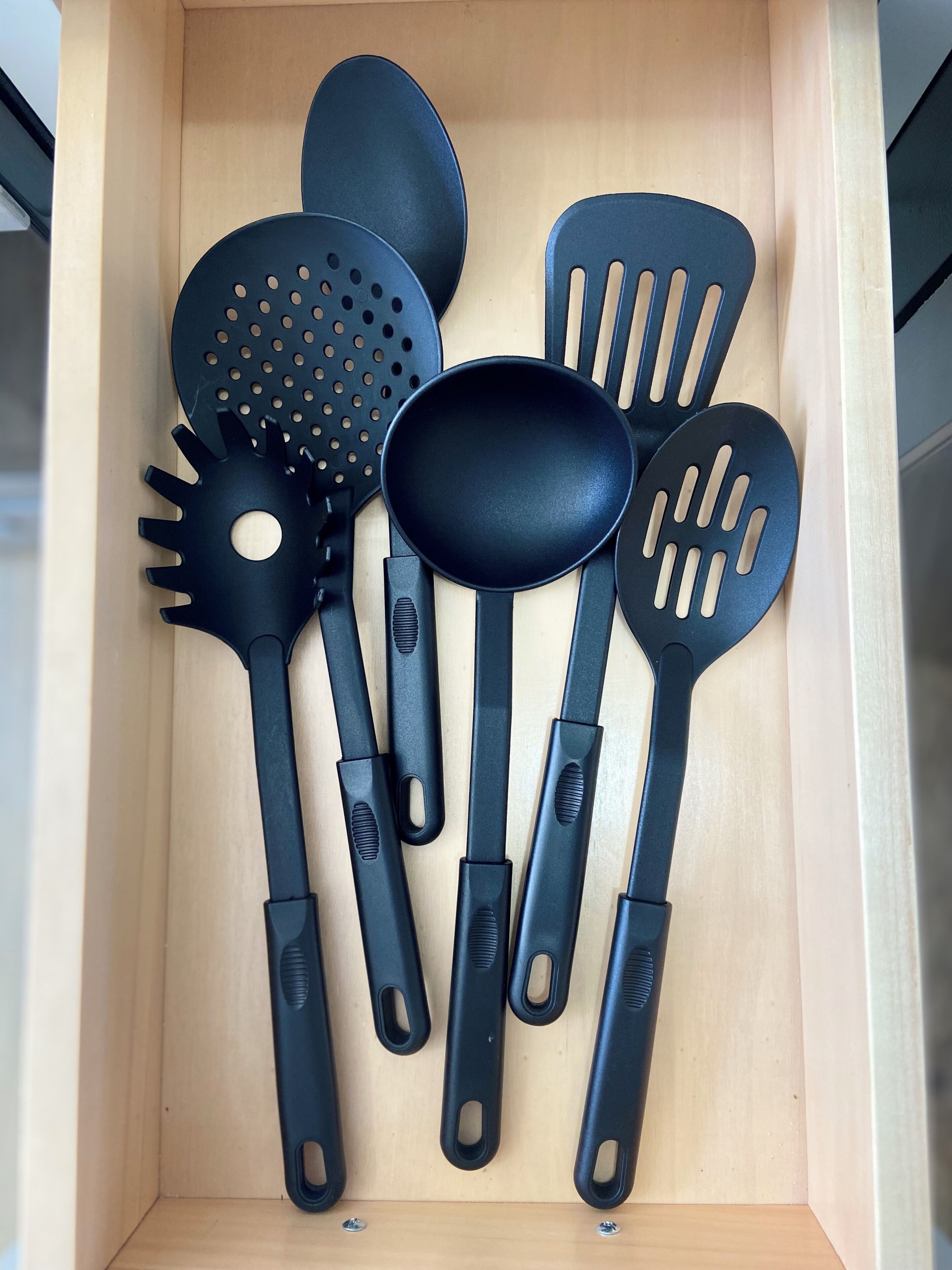 Un cajón con varios utensilios de cocina negros, como una espátula, una cuchara grande y un colador.