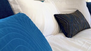 Un lit avec une literie blanche et bleue, une tête de lit bleue et un tableau abstrait aux couleurs vives accroché au mur.