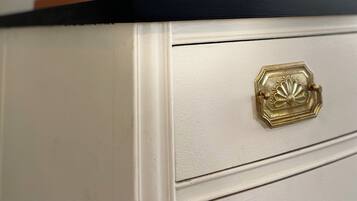 A white dresser with a black top, a gold handle, and a small green plant in a glass container.