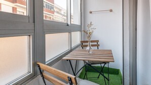 Una habitación con ventana, una mesa con sillas, un banco y una planta pequeña.