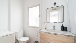 Un baño con inodoro, lavamanos con espejo, ventana y cubo de basura.