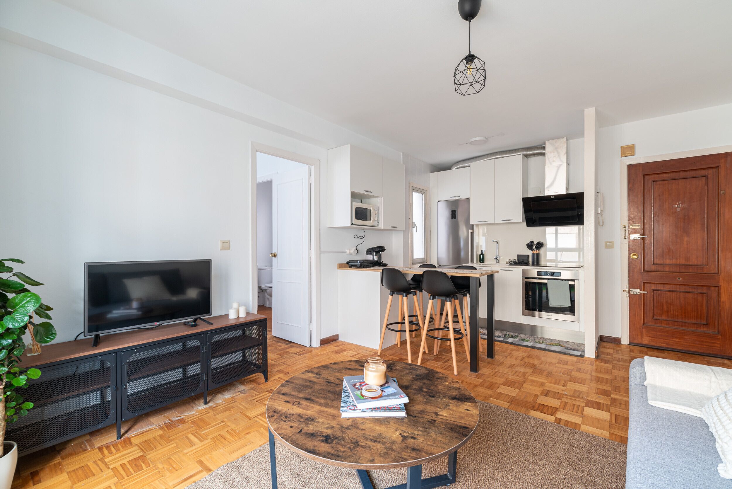 Een moderne woonkamer met een flatscreen televisie, een ronde salontafel en een eethoek met stoelen.