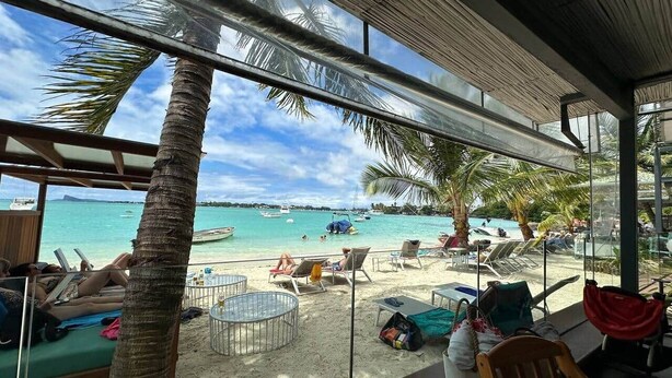Un área de descanso frente a la playa con vista al océano, palmeras y sillones.