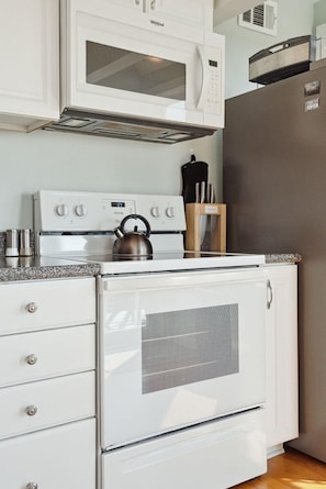 Une cuisine équipée d’une cuisinière blanche, d’un four à micro-ondes et d’un réfrigérateur, ainsi que d’une bouilloire et d’un bloc à couteaux.