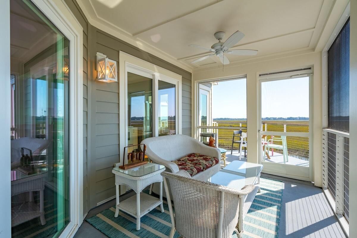 A covered outdoor area with wicker furniture, a ceiling fan, and large windows offering a view.