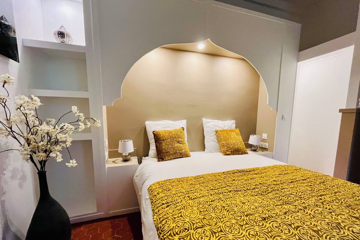 A hotel room with a large bed, two bedside tables, a nightstand, a vase with flowers, and a decorative wall panel.