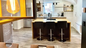 A modern kitchen with a central island, bar stools, and a hanging light fixture.
