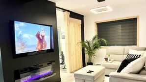 A modern living room with a flat-screen TV, a grey sofa, a wooden coffee table, and a potted plant.