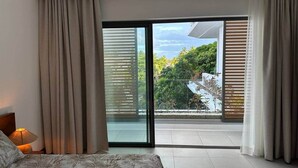 A bedroom with a bed, a nightstand, and a view of a balcony with a glass door.