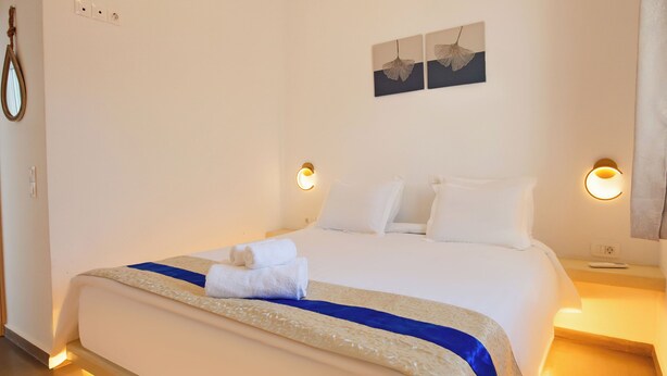 A hotel room with a neatly made bed, two wall-mounted light fixtures, and a ceiling light fixture. - Eutixia house,Santorini  (santorini)