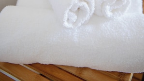 A stack of white towels on a wooden surface in a bathroom with a hairdryer and a towel rack in the background. - Eutixia house,Santorini  (santorini)