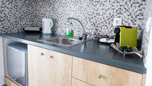 A kitchen with a tiled backsplash, a sink, a coffee maker, a toaster, and a dish rack with cups. - Eutixia house,Santorini  (santorini)