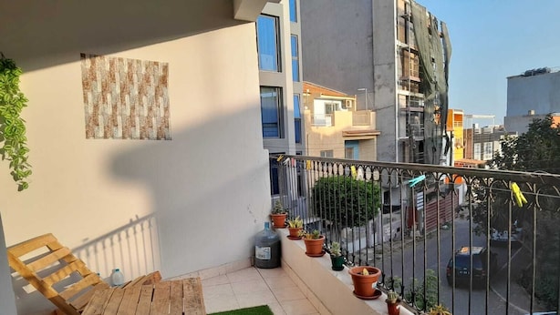 A balcony with a wooden table and chairs, potted plants, and a view of the street. - The Hidden One (Praia)