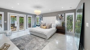A modern bedroom with a large bed, a chandelier, and a view of the outdoors through the sliding doors.