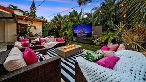 An outdoor seating area with wicker furniture, a fire feature, and a TV screen displaying 'Walt Disney Studios'.