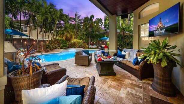 A poolside area with wicker furniture, a pool, and a Disney-themed TV. - 5 Bedroom Luxury Home, Minutes to Las Olas, Shops & Beach (Fort Lauderdale)