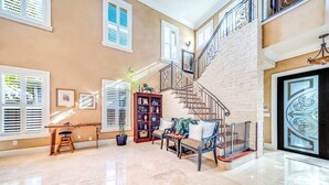 A spacious living area with a high ceiling, a staircase with metal railings, and a large window with blinds. - 5 Bedroom Luxury Home, Minutes to Las Olas, Shops & Beach (Fort Lauderdale)