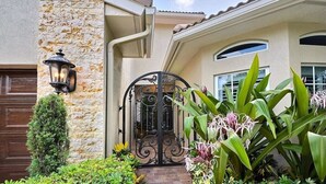 A house with a stone facade, a metal gate, and a well-maintained garden with various plants. - 5 Bedroom Luxury Home, Minutes to Las Olas, Shops & Beach (Fort Lauderdale)