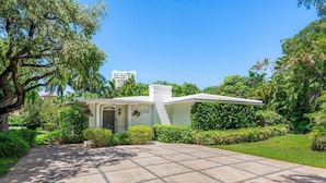 A white building with a central tower, surrounded by lush greenery and a paved driveway.