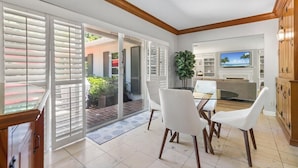 A modern kitchen with white cabinets, a glass dining table, and a TV.