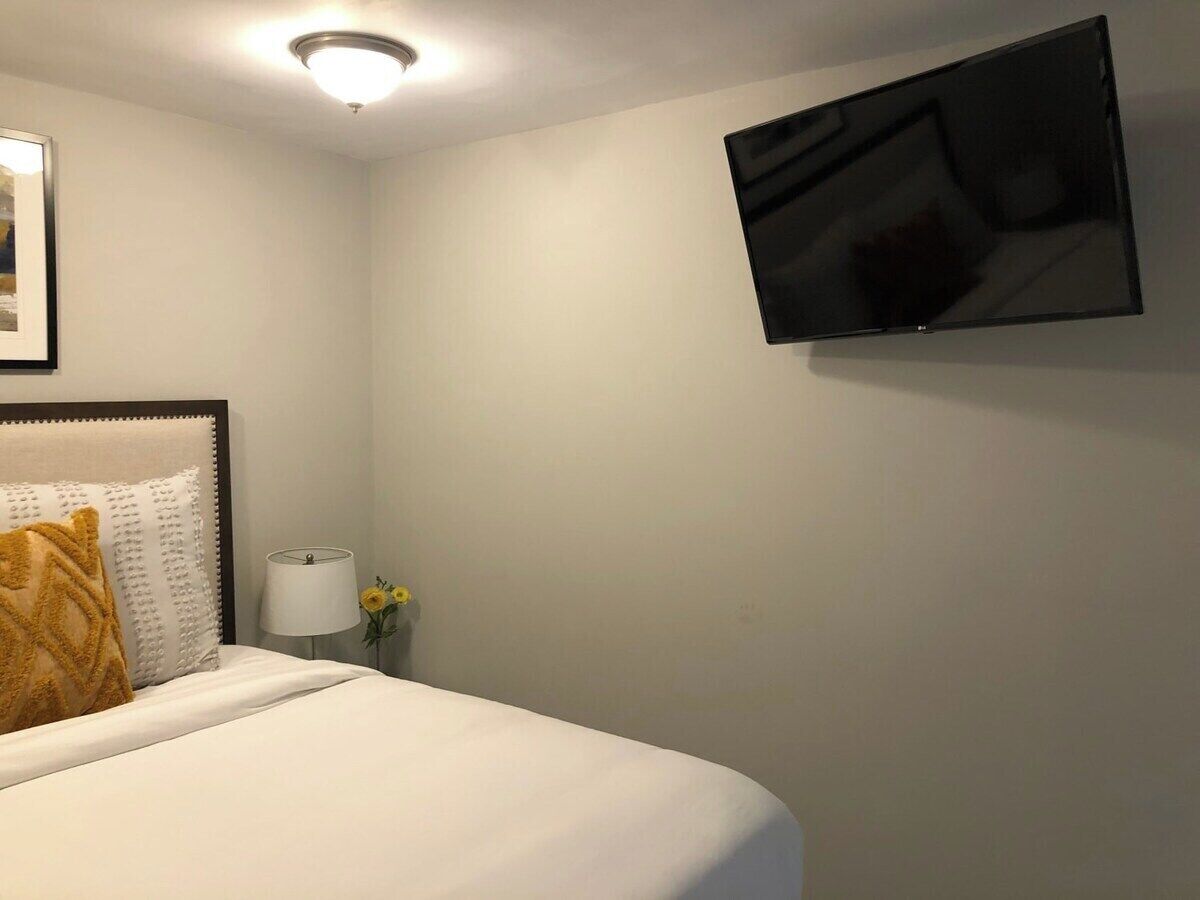 A hotel room with a bed, a bedside lamp, a TV mounted on the wall, and a framed picture on the wall.