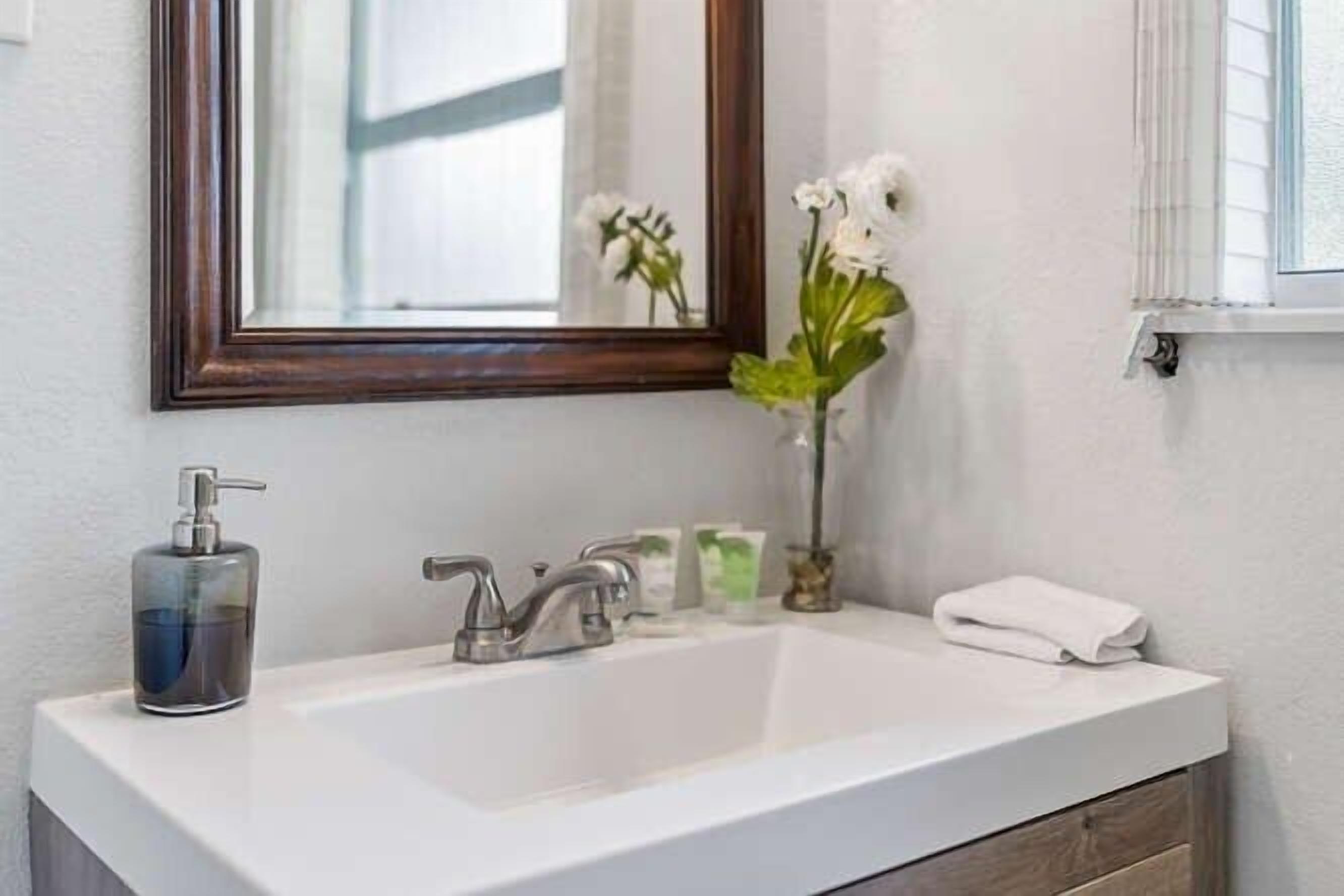 A bathroom with a white sink, a mirror, a vase with flowers, and toiletries.
