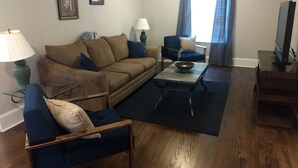 A living room with a brown sofa, blue armchairs, a coffee table, and a TV stand. - Spacious 4BR/2.5BA•Pet-Friendly•Safe Charlotte Location Near Uptown & SouthPark! (Charlotte)