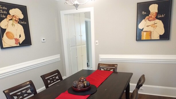 A dining room with a dark wooden table, red runner, and six chairs. Two framed posters adorn the walls. - Spacious 4BR/2.5BA•Pet-Friendly•Safe Charlotte Location Near Uptown & SouthPark! (Charlotte)