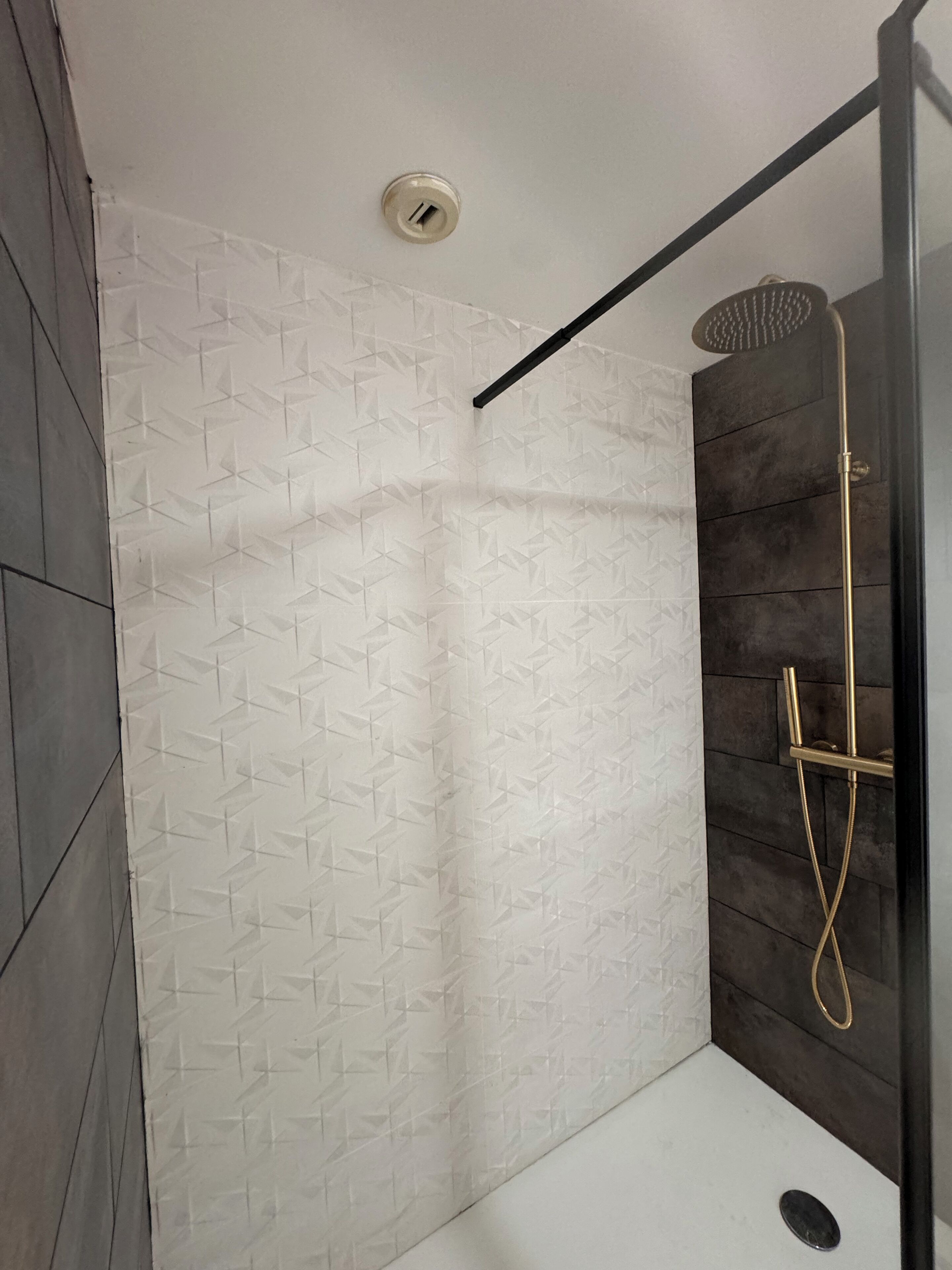 A modern shower area with a geometric tile wall, a showerhead, and a control panel.