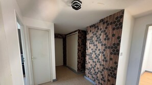Un pasillo con alfombra color beige, paredes blancas y una pared de madera con diseño hexagonal. Hay puertas a ambos lados, una que da a un armario y otra a una habitación.