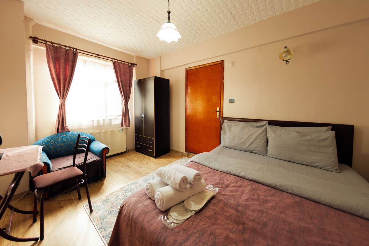 Quarto de hotel com cama, escrivaninha, cadeira, guarda-roupa e radiador.