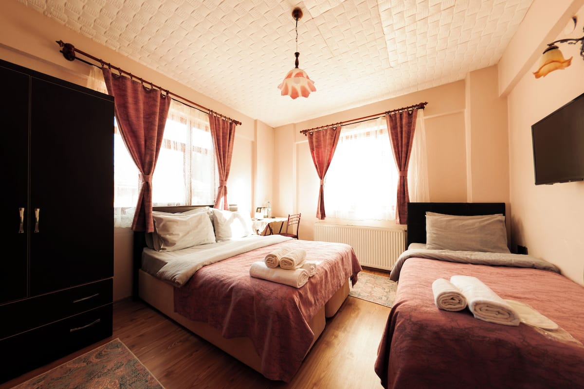 Quarto de hotel com duas camas, um guarda-roupa, uma escrivaninha e uma televisão.
