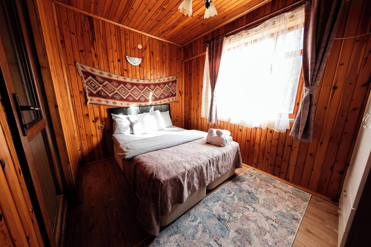 Um quarto com painéis de madeira, uma cama, um tapete estampado e uma janela com cortinas.