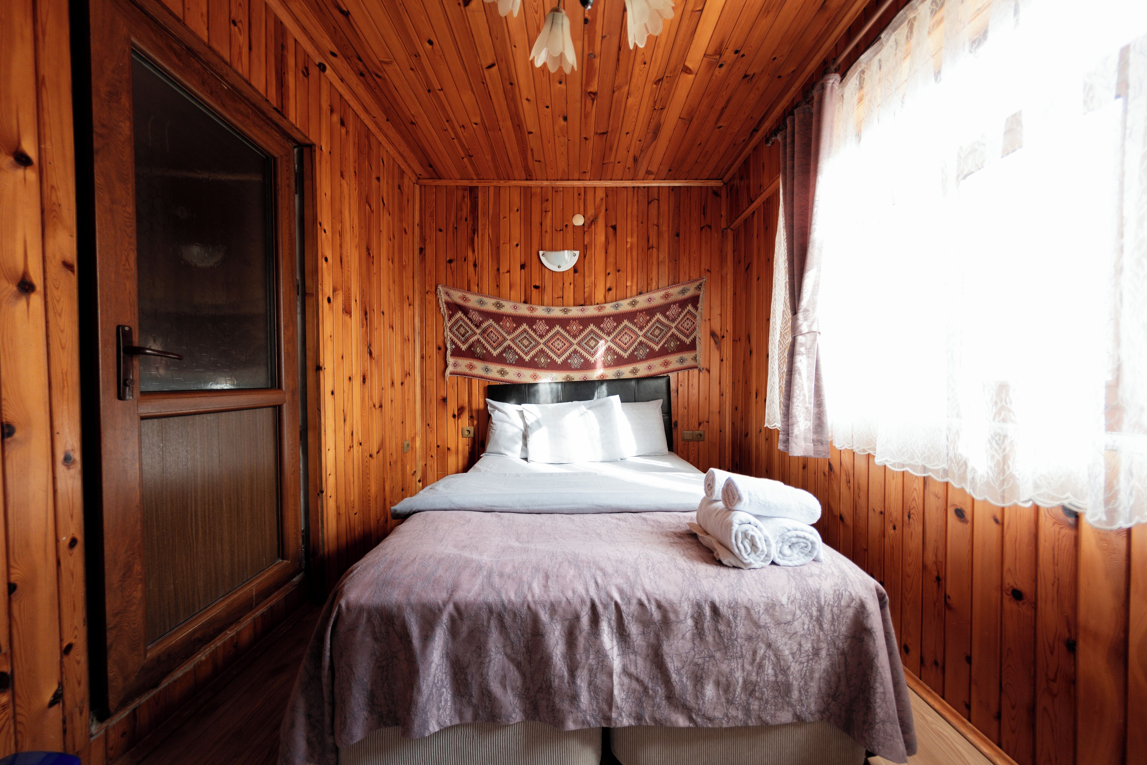 A wooden-paneled room with a bed, a door, and a window with curtains.