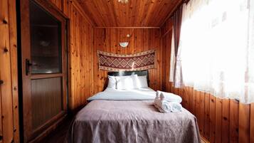 A wooden-paneled room with a bed, a door, and a window with curtains.