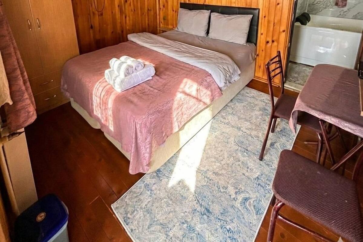 Quarto com painéis de madeira, cama, televisão, mesa pequena e cadeira.