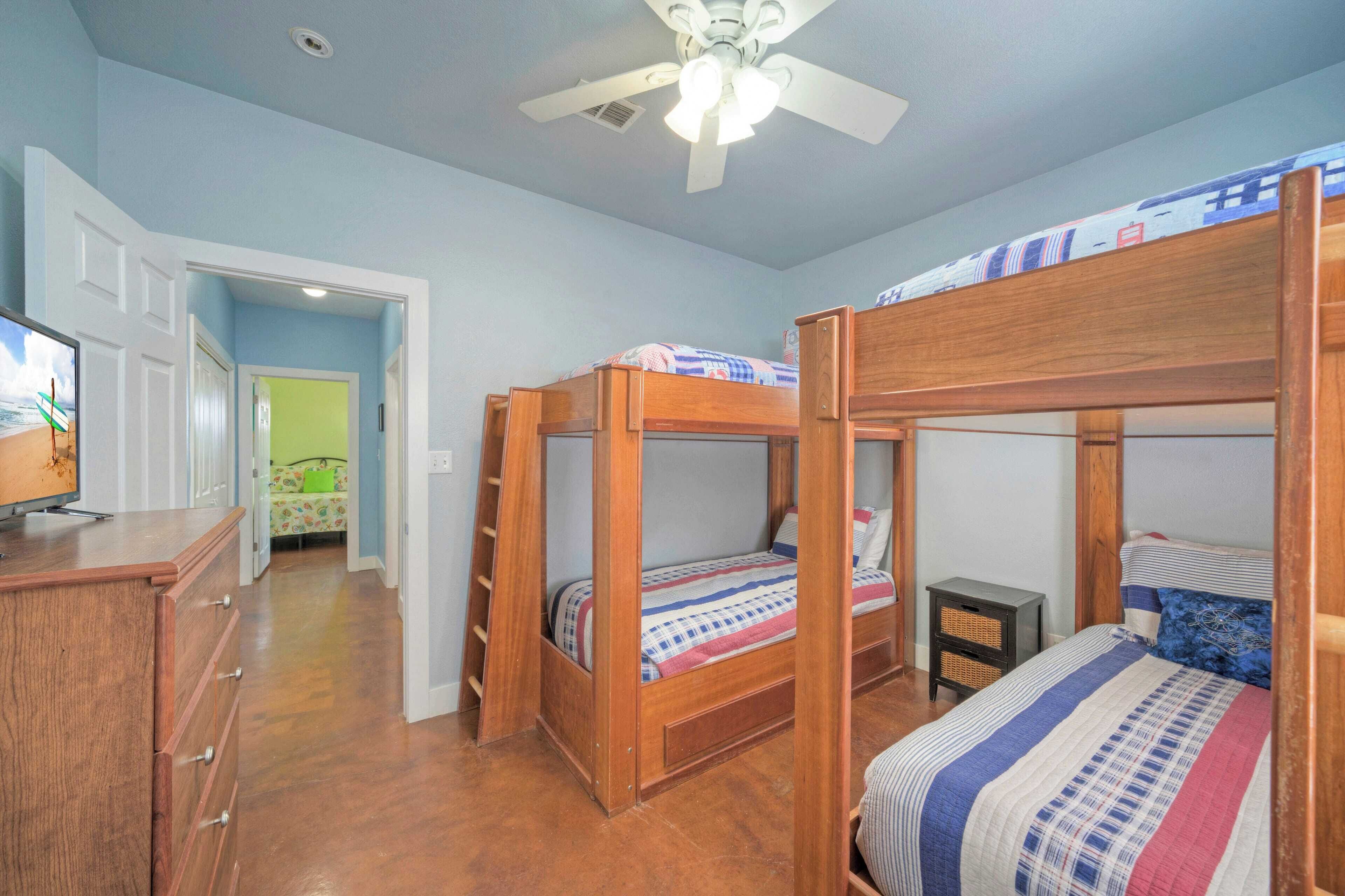 Une chambre avec des lits superposés, une commode en bois, un téléviseur et un ventilateur de plafond.