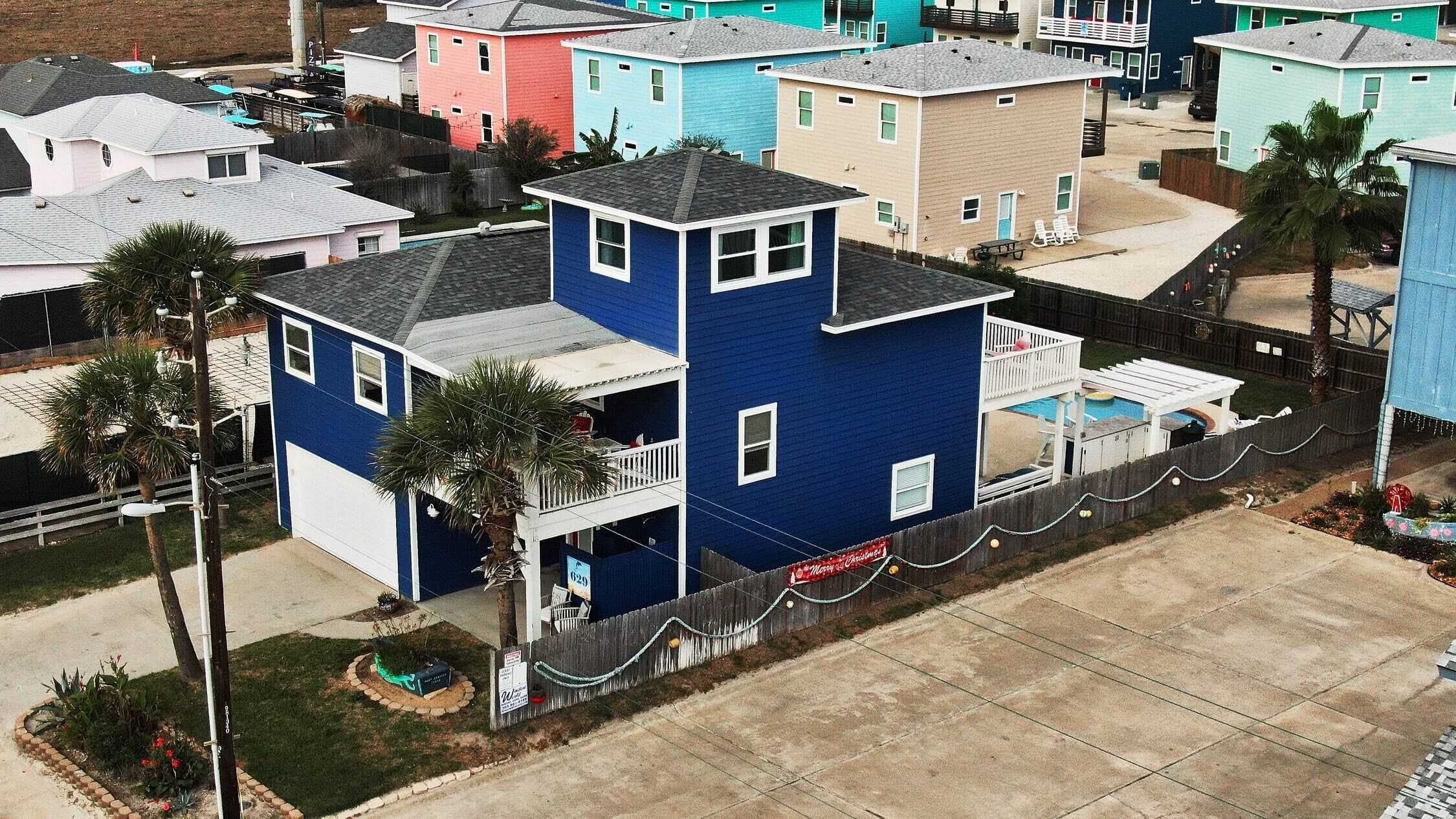 A two-story house with a blue exterior, a balcony, and a small front yard with a palm tree.
